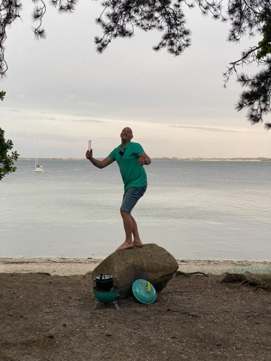 David steht mit einer Grillgabel in der Hand auf einem Felsen bei Sjællands Odde.